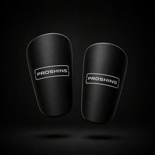 Pair of black shin guards with 'Proshins' branding on a dark background